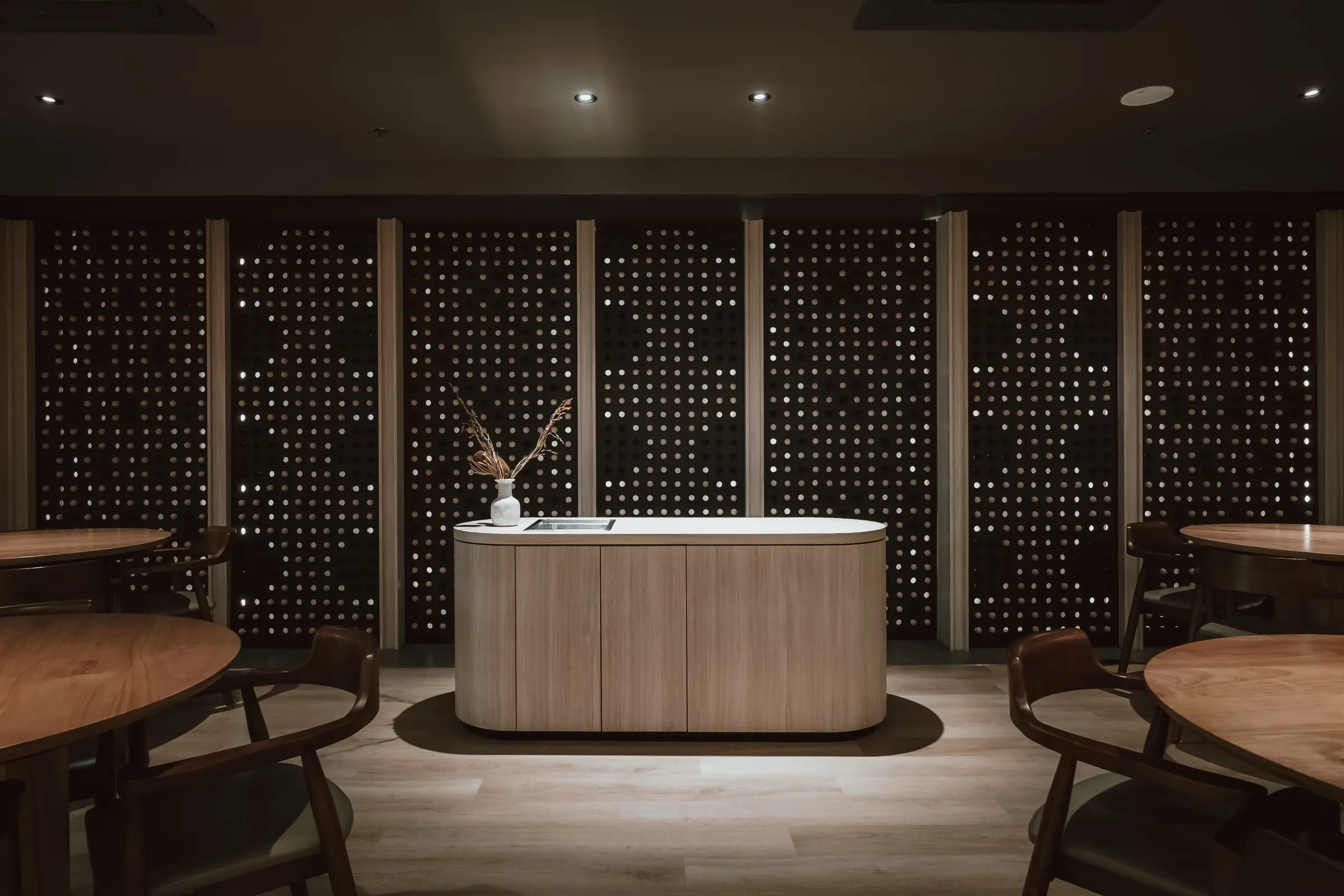 OITOM's dining room: a pale oak island under soft downlights, in front of a wall of dark panels pierced with hundreds of points of light, with round oak tables and chairs either side.